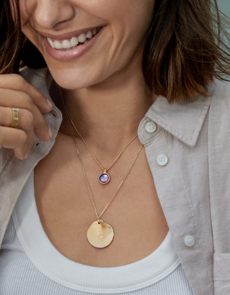 A woman wearing a gold necklace with an ombré lavender sea glass pendant