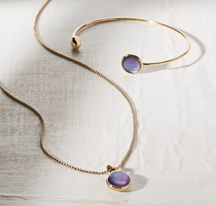 Ein Armband Sea Glass in Lavendel-Ombré und eine goldfarbene Halskette mit einem Anhänger in Lavendel-Ombré.