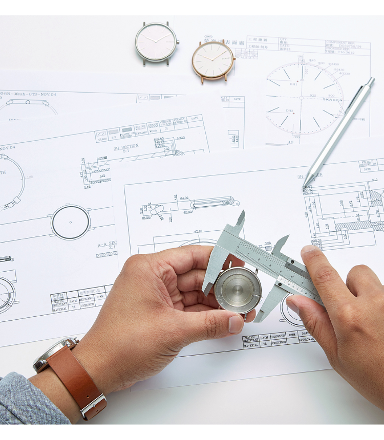 a watch designer measuring a watch case over a table of design schematics and tools