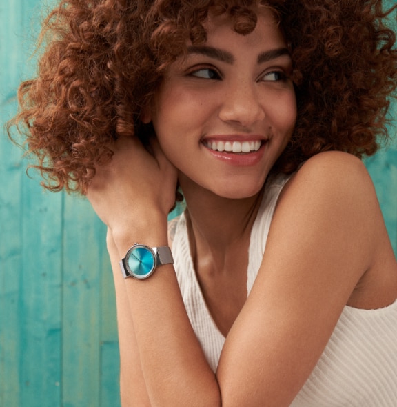 Eine Frau, die eine Uhr mit silberfarbenem Gehäuse, farblich passendem Milanaiseband und blauem Zifferblatt trägt.